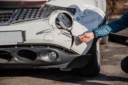 Insurance agent will examine and examine the damage to the car after an accident. Inspection of the car after an accident on the road. The front fender and right headlight are broken, damaged and scratched on the bumper.の写真素材