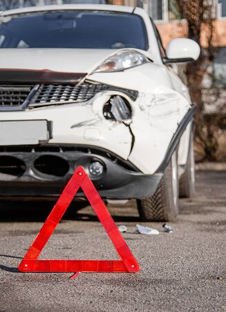 Close up car emergency stop sign on the road. Car accident or accident. The front fender and right headlight are broken, damaged and scratched on the bumper.の写真素材