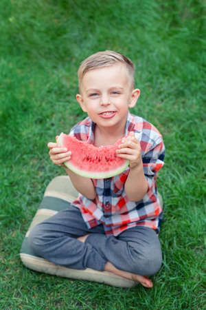 Happy child eating watermelon in the garden. Kids eat fruit outdoors. Healthy snack for children. Little boy playing in the garden biting a slice of water melon.の写真素材