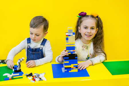 Siblings playing constructor on a yellow background.