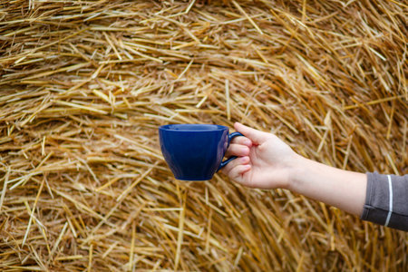 Good morning. Female hand holds a porcelain blue cup of coffee on a natural background. Selective focus on the cup.の写真素材