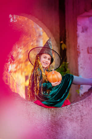 Happy halloween celebration. Beautiful girl witch with pumpkin in the park, outdoors. Little girl in halloween costume with jack pumpkin.の写真素材