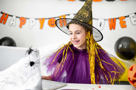 Halloween holiday concept. Cute little girl in witch costume sitting behind a table in Halloween...
