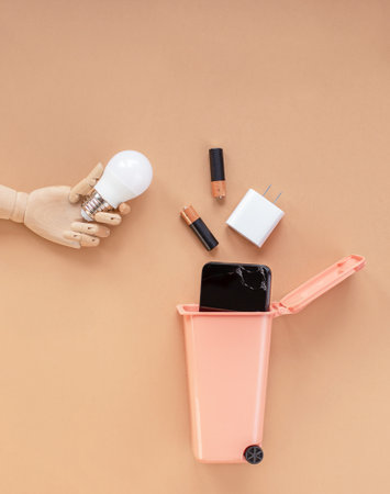 Wooden model of a hand holding a light bulb over a trash can. Garbage sorting concept. E-Waste disposal.の写真素材