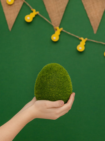Easter theme. Big egg, grass texture, in human hands on green background. Eco-friendly Easter egg.の写真素材