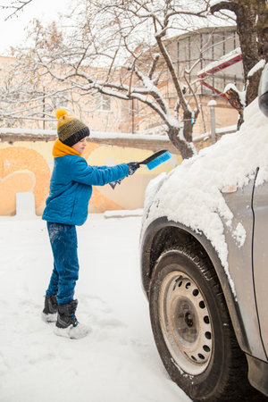 Cute little boy is helping his father brush the snow from the car. Snow removal from the car - the concept of car care during the winter.の写真素材
