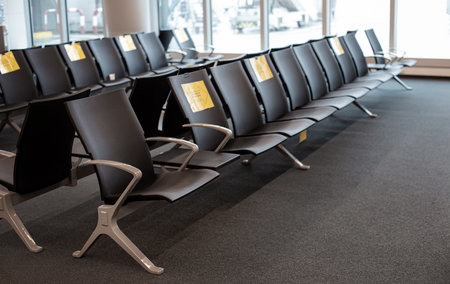 Empty airport waiting area with rows of seats and yellow signs indicating social distancing, copy spaceの写真素材