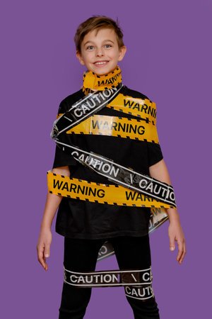 Boy stands with yellow warning tape wrapped around his body and mouth, creating a dramatic visual on bold violet background.の写真素材