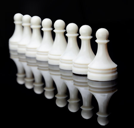 White Chess Pieces Standing in Row. Symmetrical lineup of white chess pieces on reflective surface, symbolizing strategy, balance and competition.の写真素材