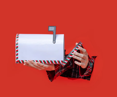Merry Christmas. Christmas themed mailbox held in two hands through a red torn paper background, with green and red striped border.の写真素材