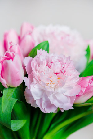 Soft pink peonies and tulips with vibrant green leaves creating fresh, elegant bouquet bursting with natural beauty and delicate floral details.