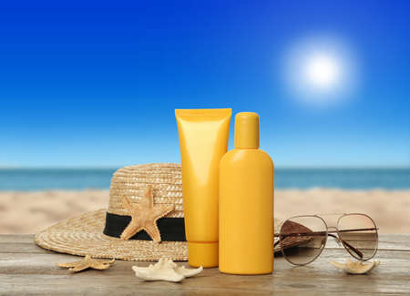 Skin sun protection products and beach accessories on wooden table against seascape. Space for...