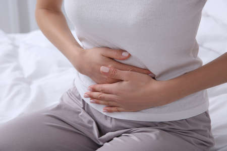 Young woman suffering from stomach ache on bed, closeupの写真素材