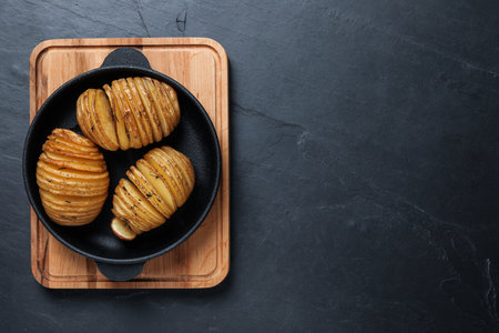 Delicious homemade Hasselback potatoes on black table, top view. Space for textの写真素材