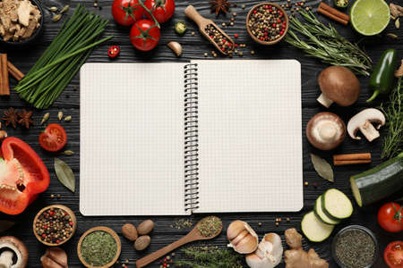 Open recipe book and different ingredients on black wooden table, flat lay. Space for textの写真素材