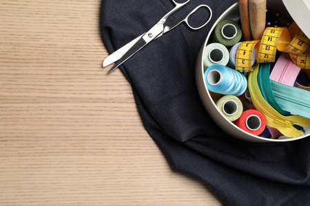 Flat lay composition with different sewing accessories on wooden background. Space for text