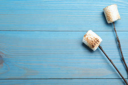 Sticks with roasted marshmallows on light blue wooden table, flat lay. Space for text