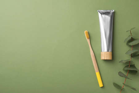 Bamboo toothbrush, tube of paste and space for text on green background, flat lay. Conscious consumptionの写真素材