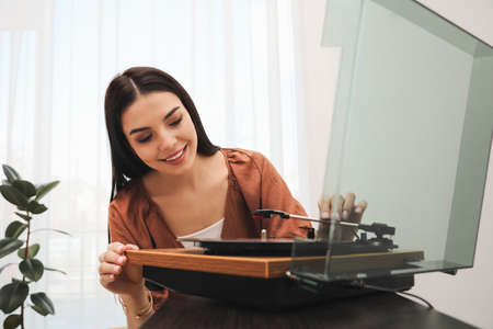 Happy young woman using turntable at home