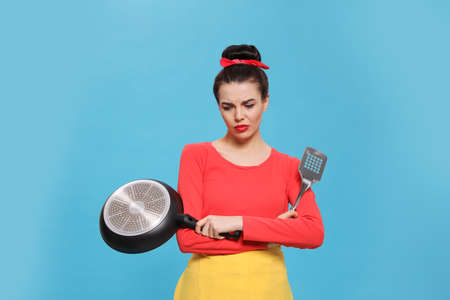 Housewife with frying pan and spatula on light blue backgroundの写真素材