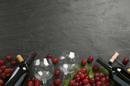 Bottles of red wine, glasses and grapes on black table, flat lay. Space for textの写真素材
