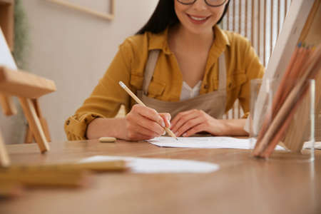 Young woman drawing with pencil at table indoors, closeupの写真素材