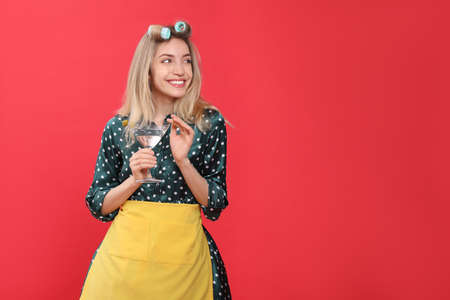 Young housewife with glass of martini on red background. Space for textの写真素材