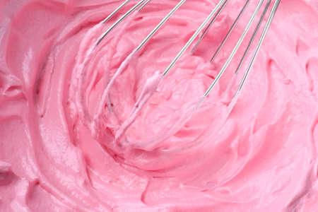 Whipping pink cream with balloon whisk, closeup view