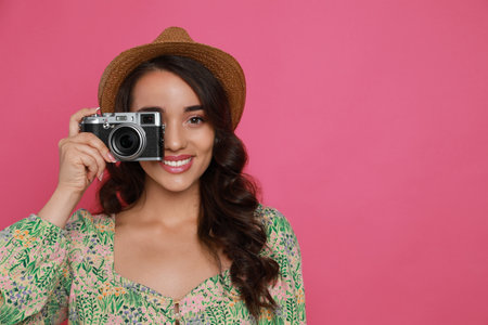 Beautiful young woman with straw hat and camera on pink background. Space for text
