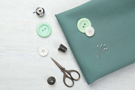 Flat lay composition with different sewing supplies and fabric on white wooden table