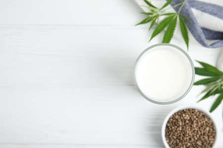 Glass of fresh hemp milk, seeds and leaves on white wooden table, flat lay. Space for textの写真素材