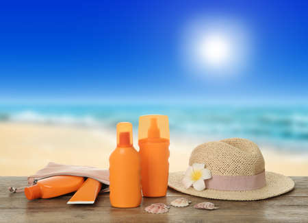 Different skin sun protection products and hat on wooden table against seascape. Space for designの写真素材