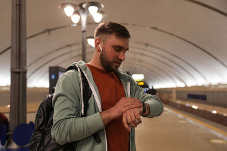 Young man with backpack and earphones waiting for train at subway station. Public transportの写真素材