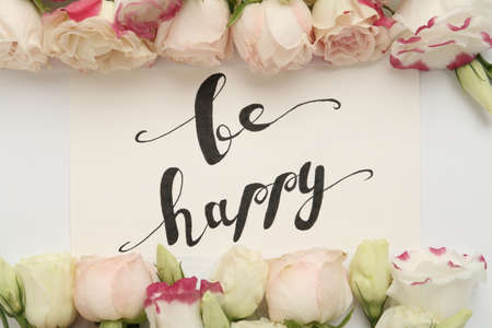 Frame of beautiful flowers and paper card with handwritten text Be happy on white background, flat layの写真素材