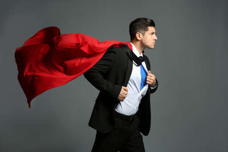 Businessman in superhero cape taking suit off on grey backgroundの写真素材