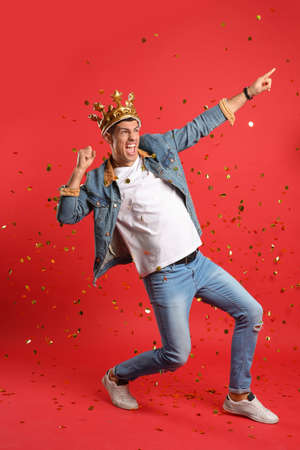 Happy man in party crown and confetti on red backgroundの写真素材