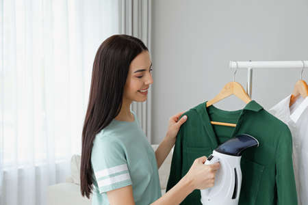 Woman steaming shirt on hanger at homeの写真素材