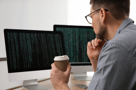 Programmer with coffee working at desk in officeの写真素材