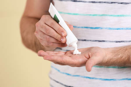 Man applying cream from tube onto hand on beige background, closeup