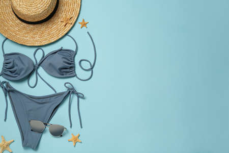 Stylish bikini, straw hat, sunglasses and starfishes on light blue background, flat lay. Space for...