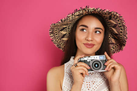 Beautiful young woman with straw hat and camera on crimson background, space for text. Stylish headdressの写真素材