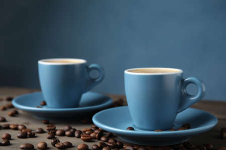 Cups of tasty espresso and scattered coffee beans on wooden tableの写真素材