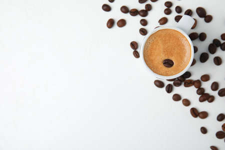 Cup of tasty espresso and scattered coffee beans on white table, flat lay. Space for textの写真素材