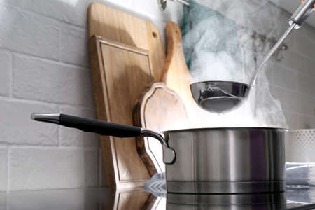 Adding water with ladle into steaming saucepan on stove in kitchen