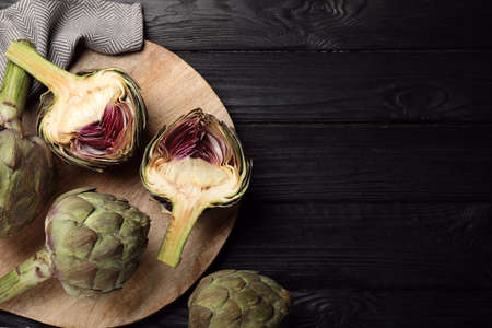 Cut and whole fresh raw artichokes on black wooden table, flat lay. Space for textの写真素材