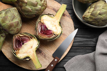 Cut and whole fresh raw artichokes on black wooden table, flat layの写真素材