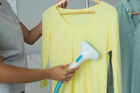 Woman steaming shirt on hanger at home, closeupの写真素材