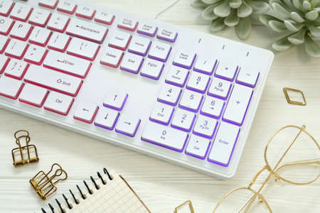 Modern RGB keyboard and eyeglasses on white wooden table
