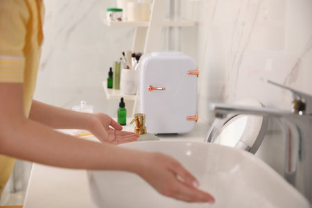 Woman washing hands near cosmetic refrigerator in bathroomの写真素材
