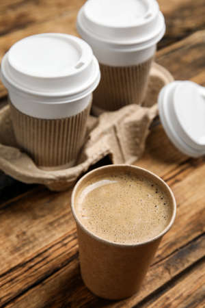 Takeaway paper cups with coffee and cardboard holder on wooden table